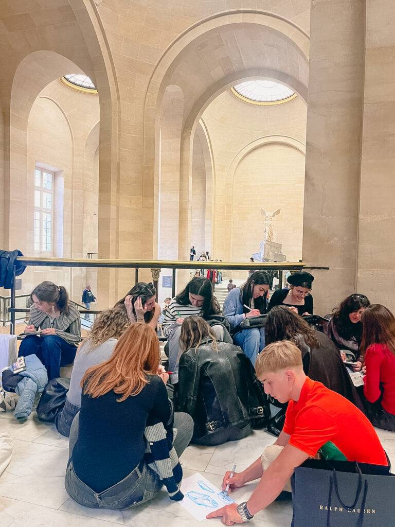 Un grupo de estudiantes se encuentra dibujando en el interior de un museo, rodeados de columnas y luz natural.