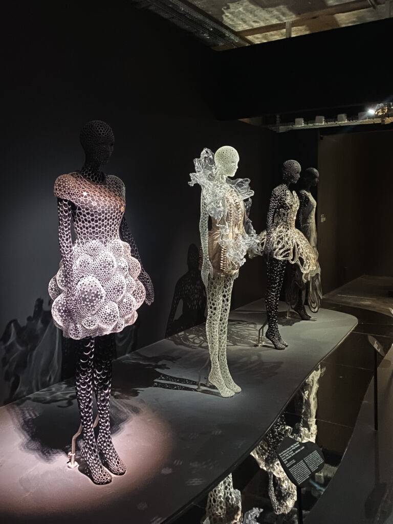 Una colección de vestidos artísticos expuestos en una galería, confeccionados con diseños futuristas y materiales innovadores.