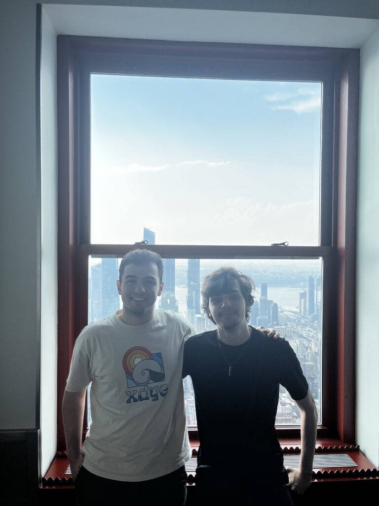 Dos personas posando frente a una ventana con vista a la ciudad.