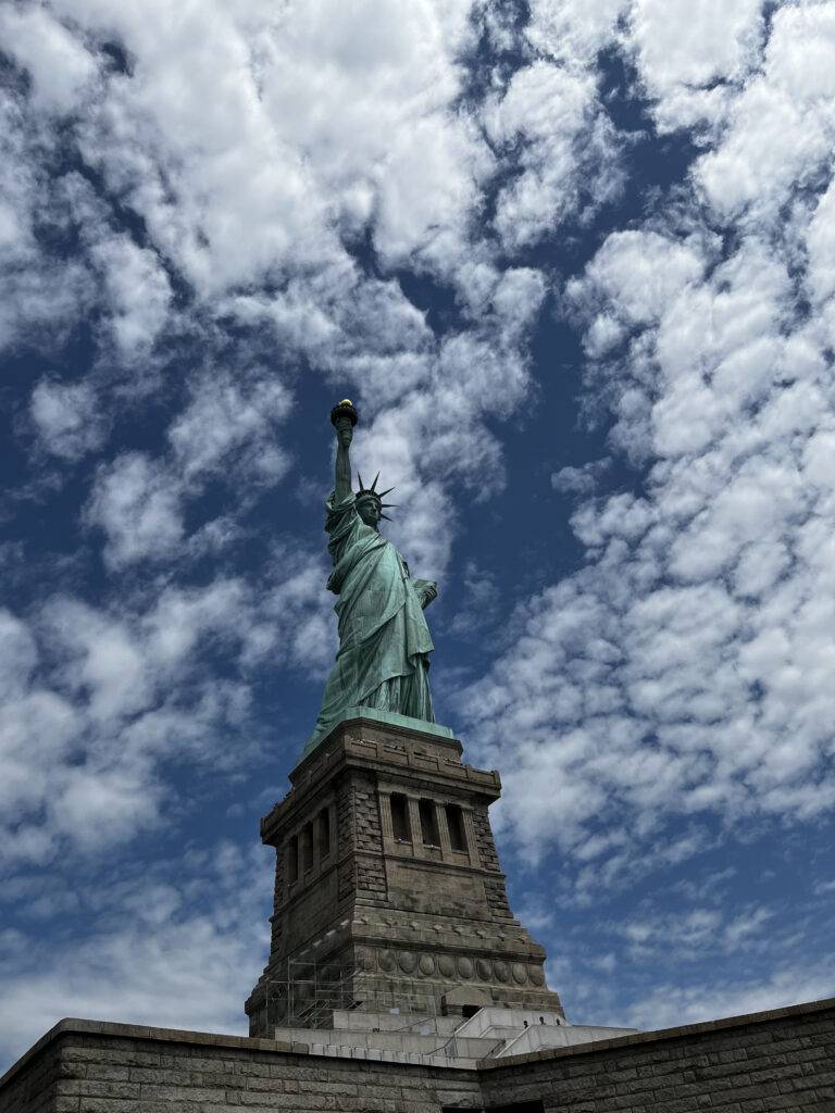 La imagen muestra la Estatua de la Libertad con un cielo nublado de fondo.
