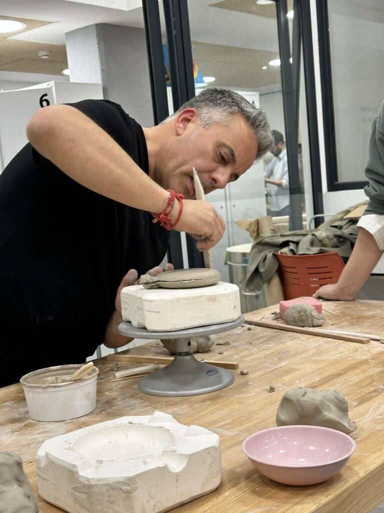 Un hombre está trabajando en el torno de alfarería, dando forma a una pieza de cerámica.