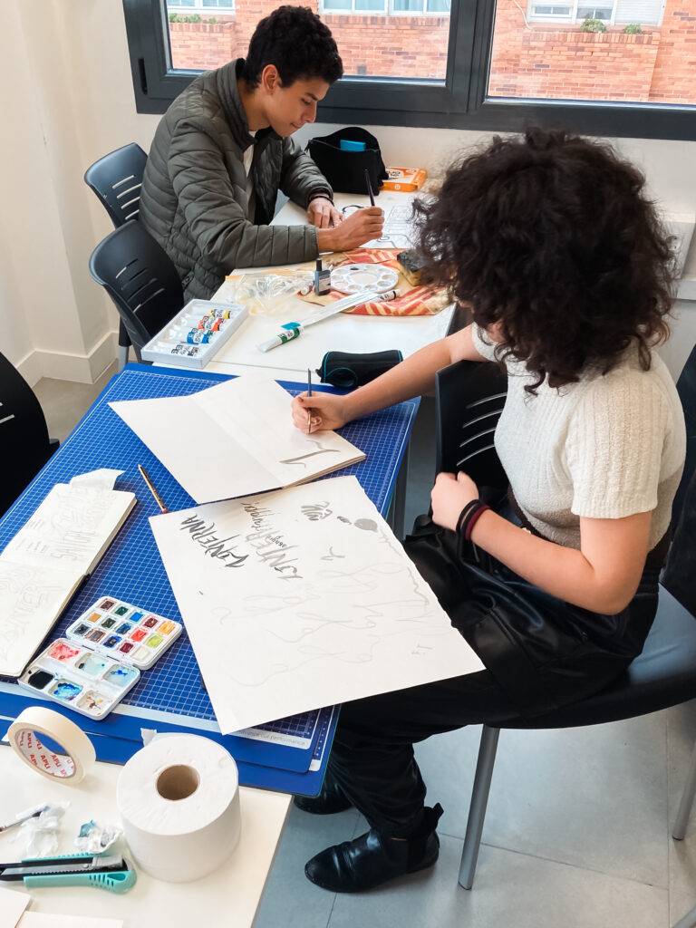 Dos personas están pintando y dibujando en una mesa de trabajo.