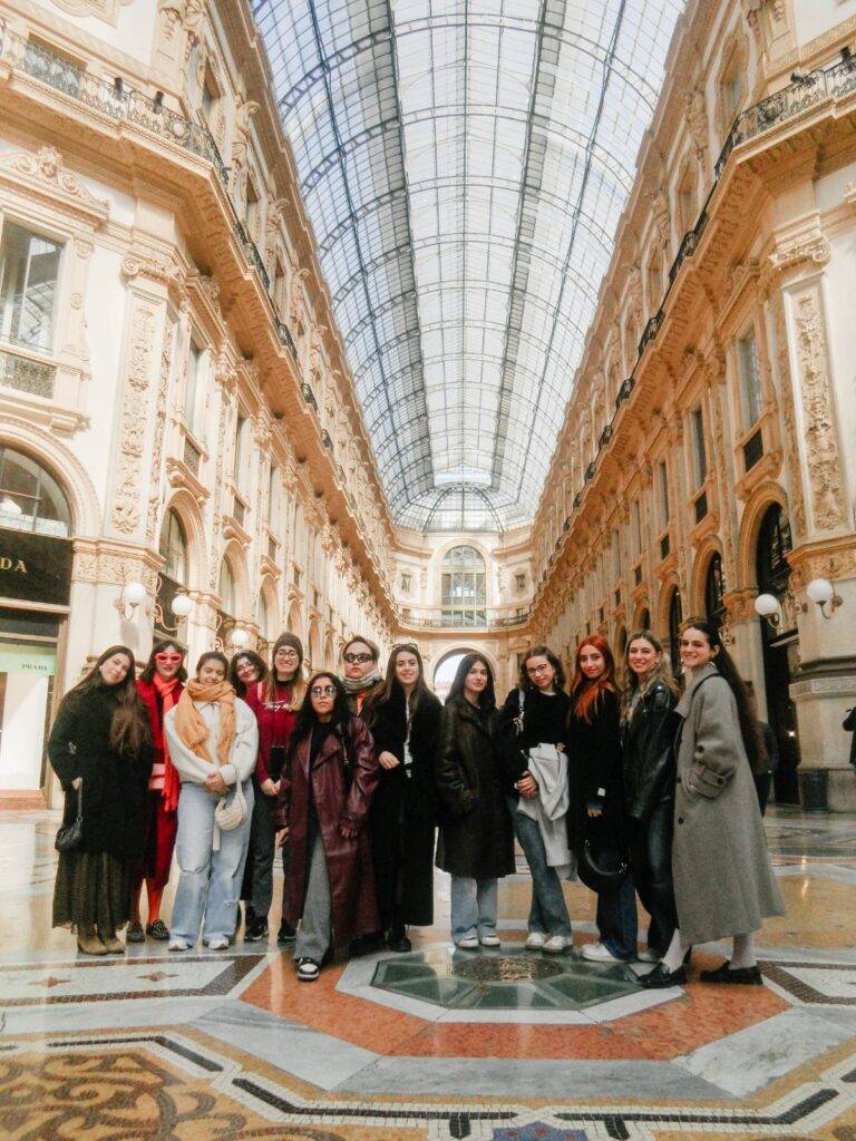 Un grupo de mujeres posa en un elegante pasillo con un techo de vidrio en un edificio histórico.