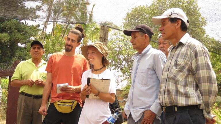 Un grupo de personas sonrientes se encuentra reunido al aire libre, conversando y observando algo en su entorno natural.