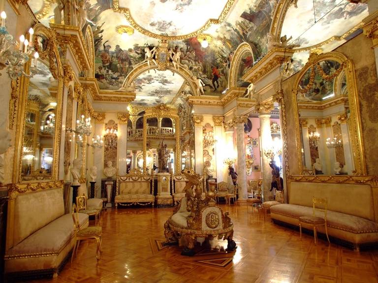 Una lujosa sala decorada con dorados y frescos en el techo.