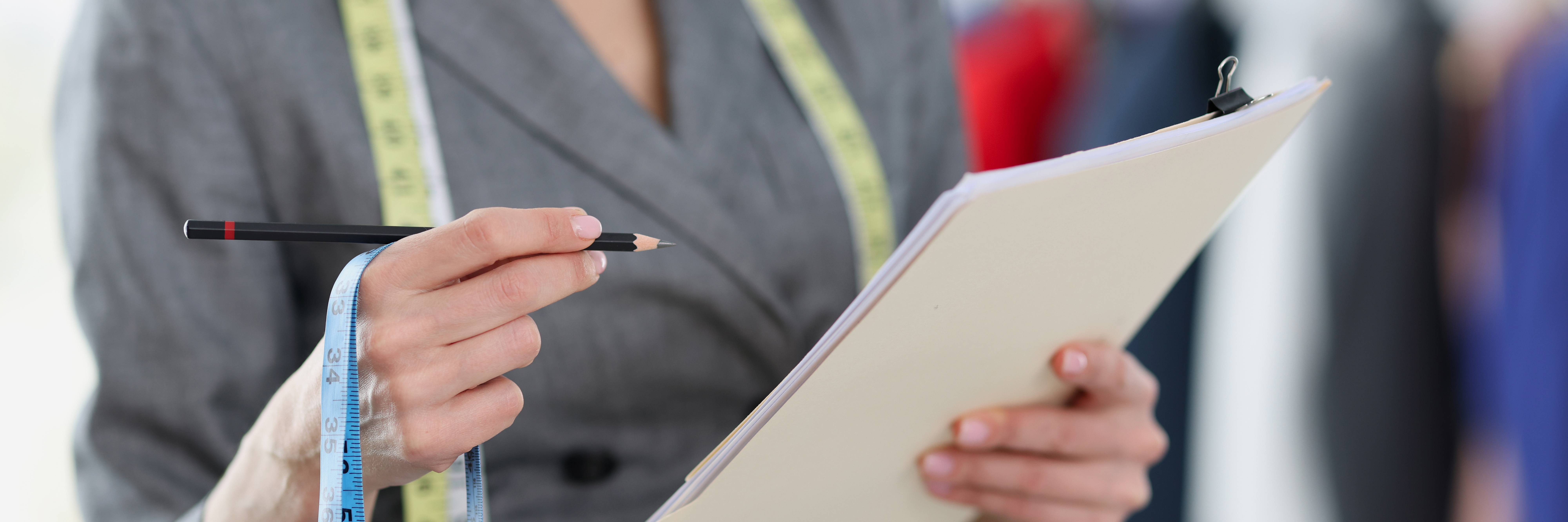 Una persona sostiene un lápiz y un cuaderno, mientras lleva una cinta métrica alrededor del cuello.
