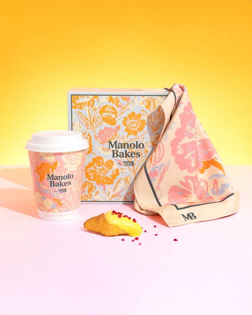 La imagen muestra un café, una caja de pastelería y una servilleta de Manolo Bakes sobre un fondo amarillo y rosa.