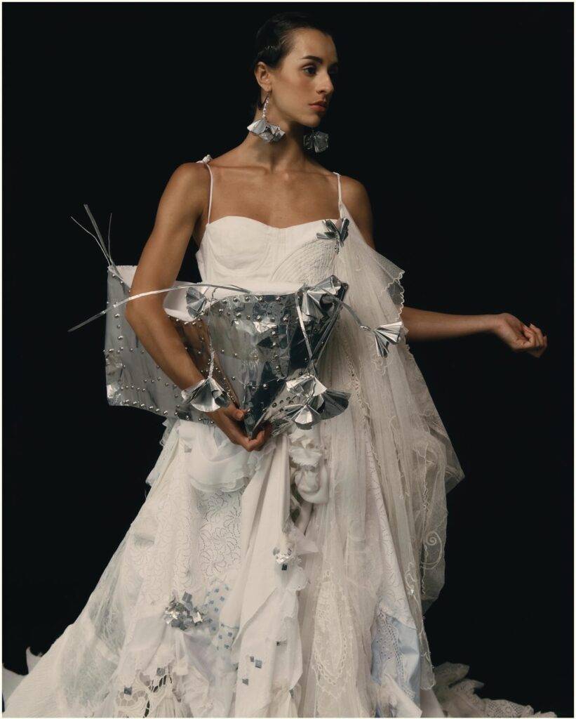 Una modelo viste un elegante vestido blanco con detalles plateados y accesorios llamativos.