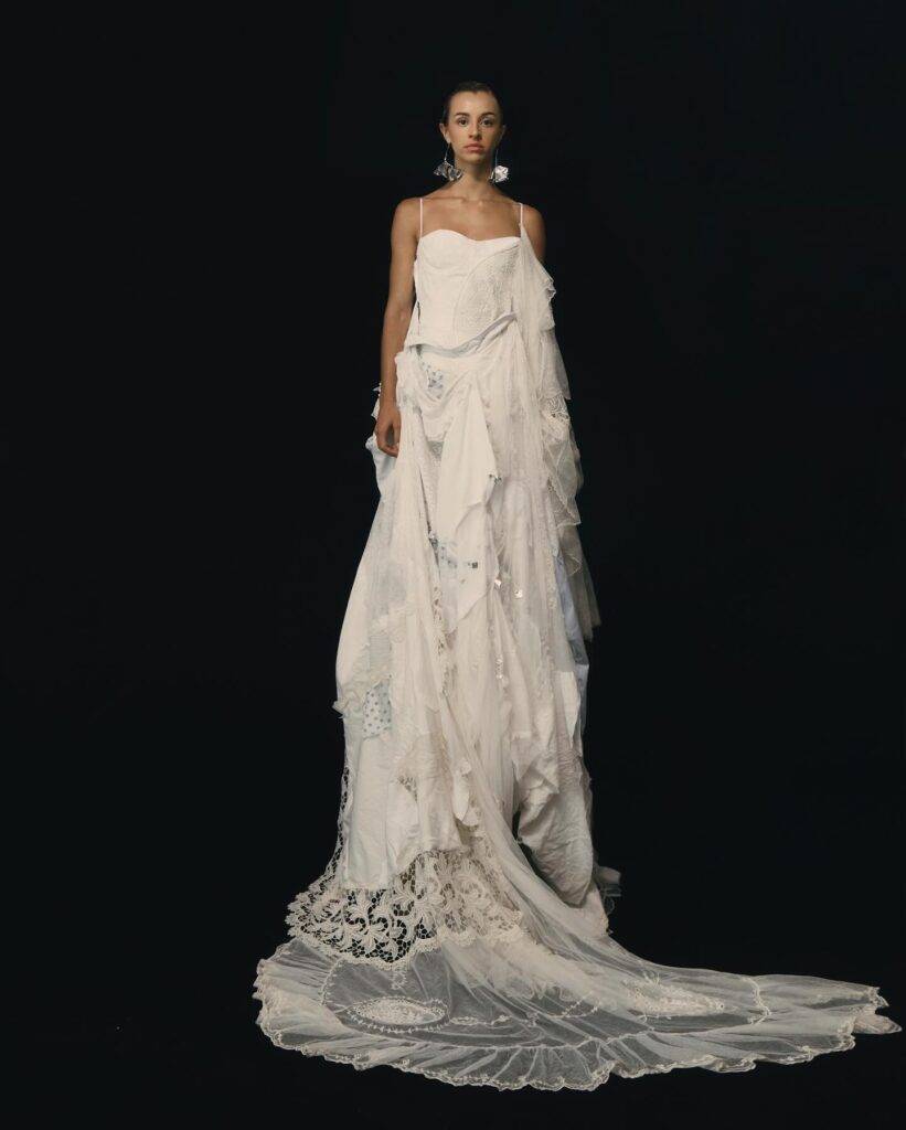 Una modelo posa con un vestido blanco elegante y vaporoso sobre un fondo negro.