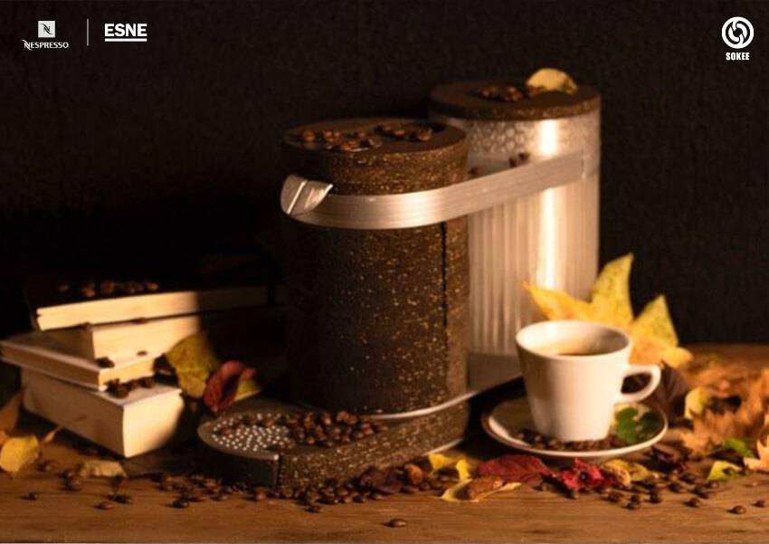 Una composición artística que presenta una taza de café junto a contenedores de café y hojas otoñales sobre una mesa de madera.