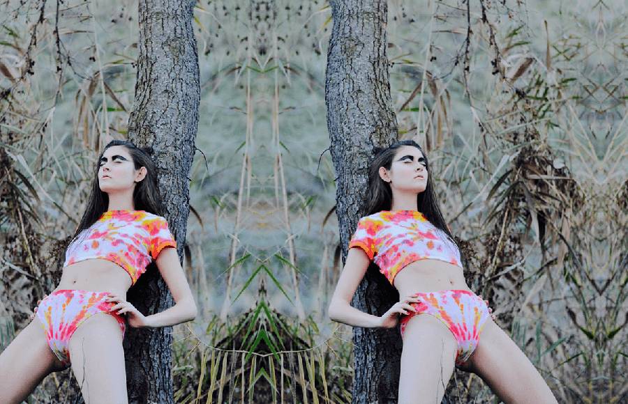 Una modelo posa de manera artística junto a un árbol en un entorno natural.