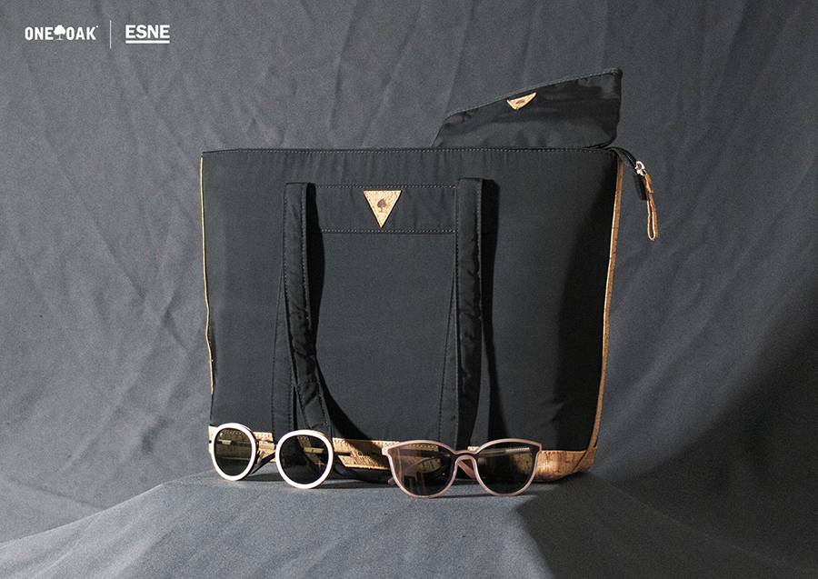Una bolsa negra con detalles en tonos beige y dos pares de gafas de sol frente a ella.