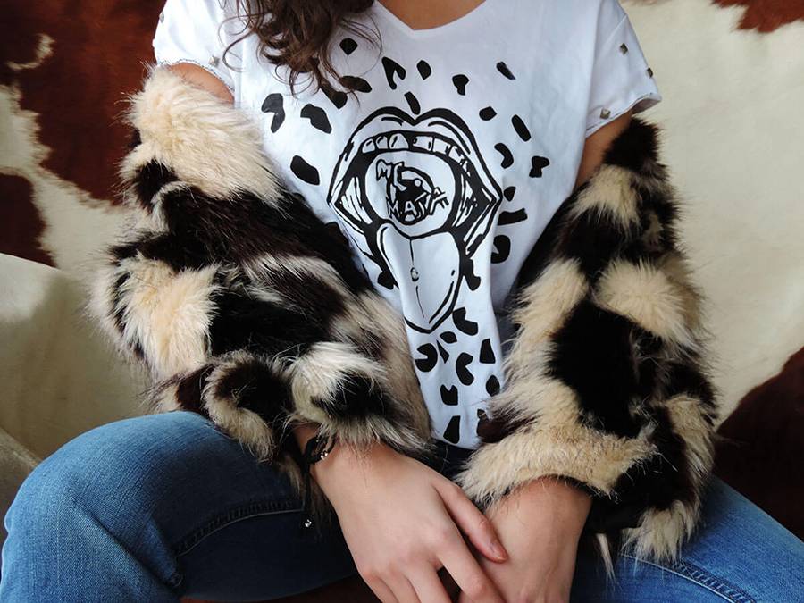 Una persona lleva una camiseta blanca con un diseño gráfico y un abrigo de pelaje de animales.