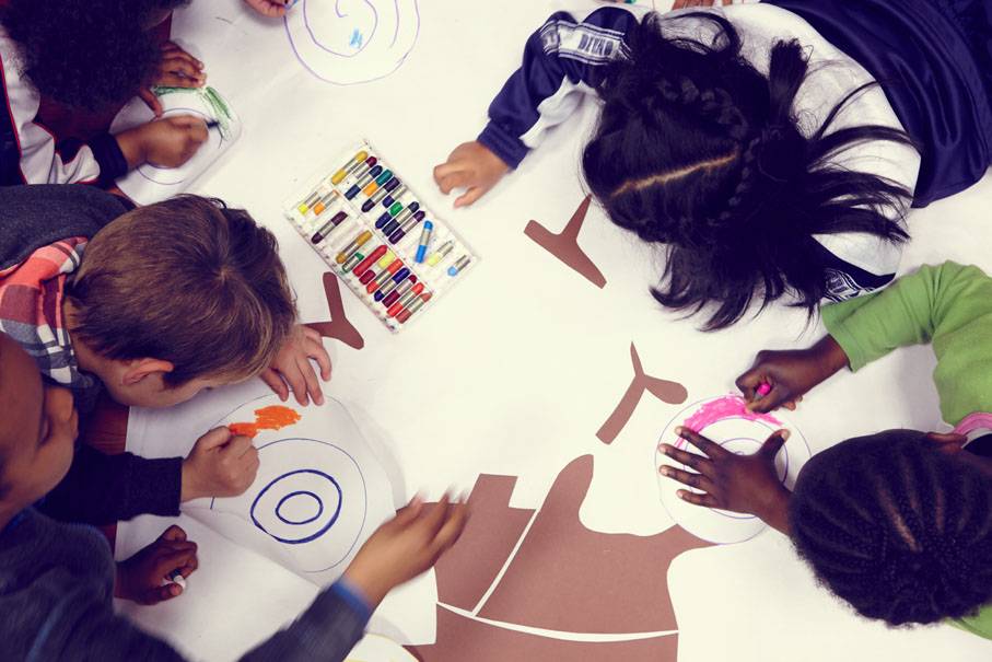 Un grupo de niños dibujando y coloreando sobre una gran superficie de papel.