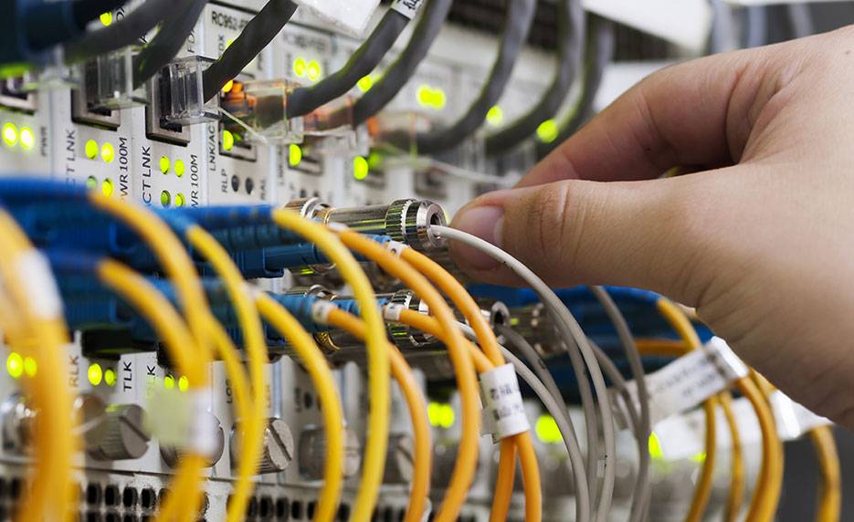 Una mano conectando cables en un panel de conexiones de red.