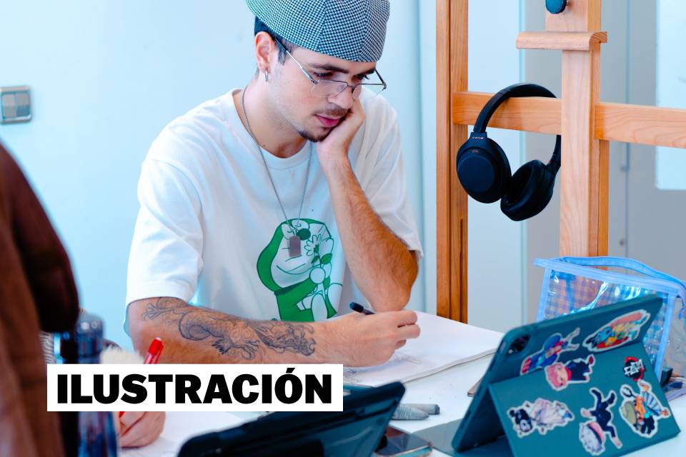 Un joven que dibuja concentrado en una mesa con varios objetos alrededor.