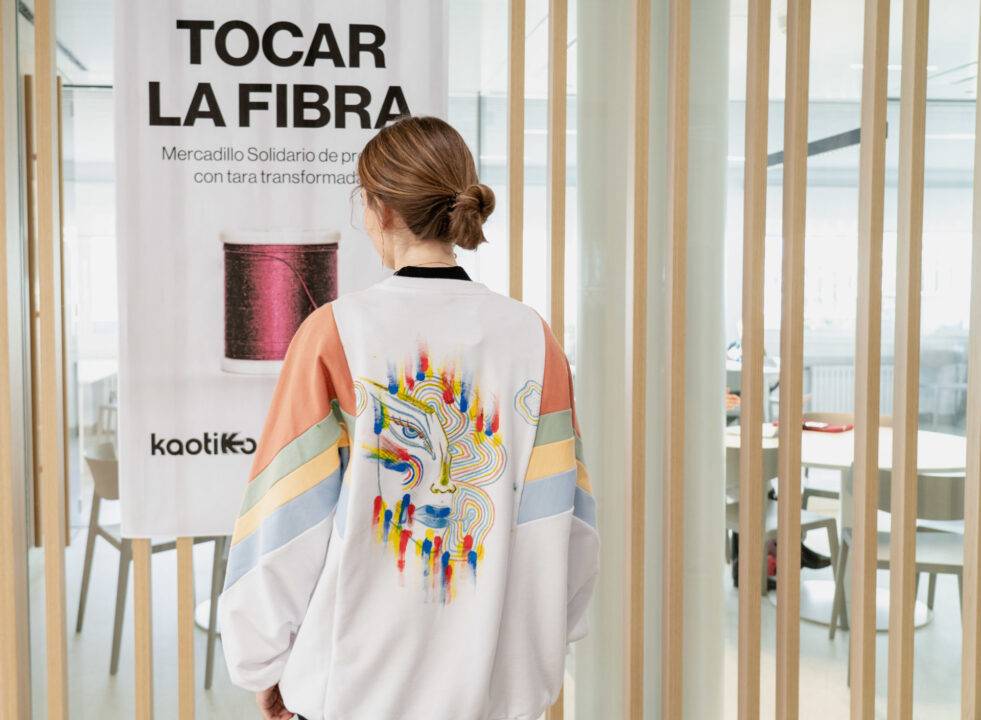 Una persona con chaqueta blanca y colorida observa un cartel que dice 'TOCAR LA FIBRA'.