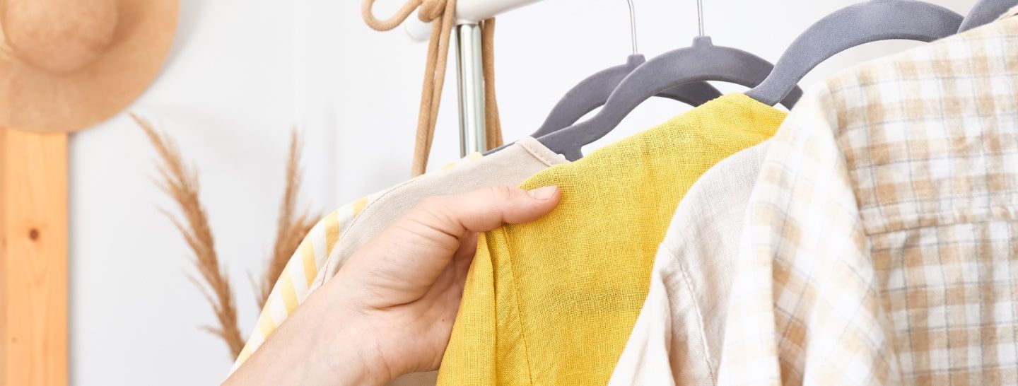 Una mano sostiene una prenda amarilla en un perchero con otras camisas de colores claros.