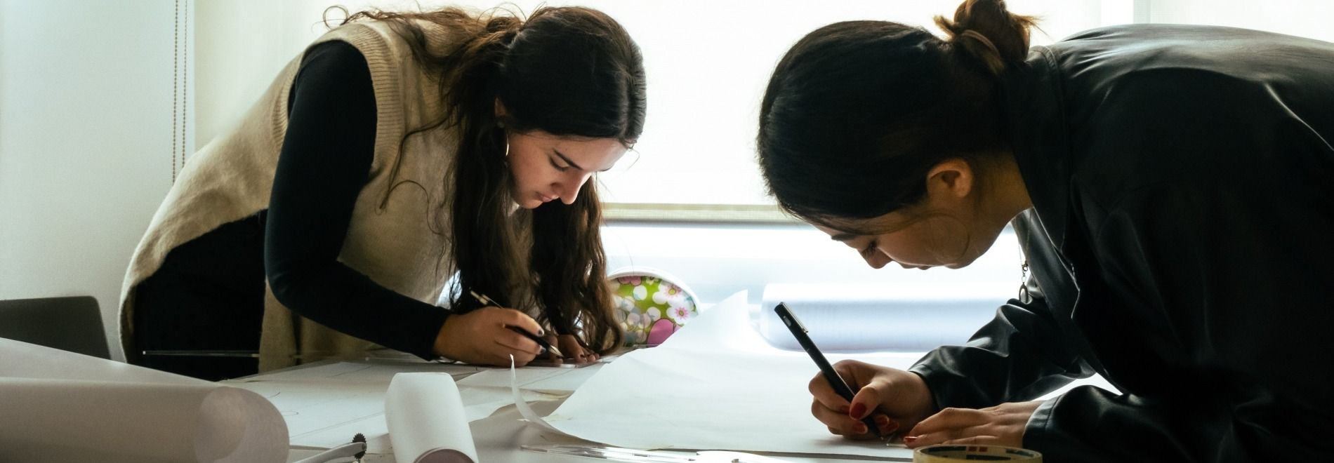 Dos personas están trabajando en un proyecto, dibujando y tomando notas sobre papeles en una mesa.