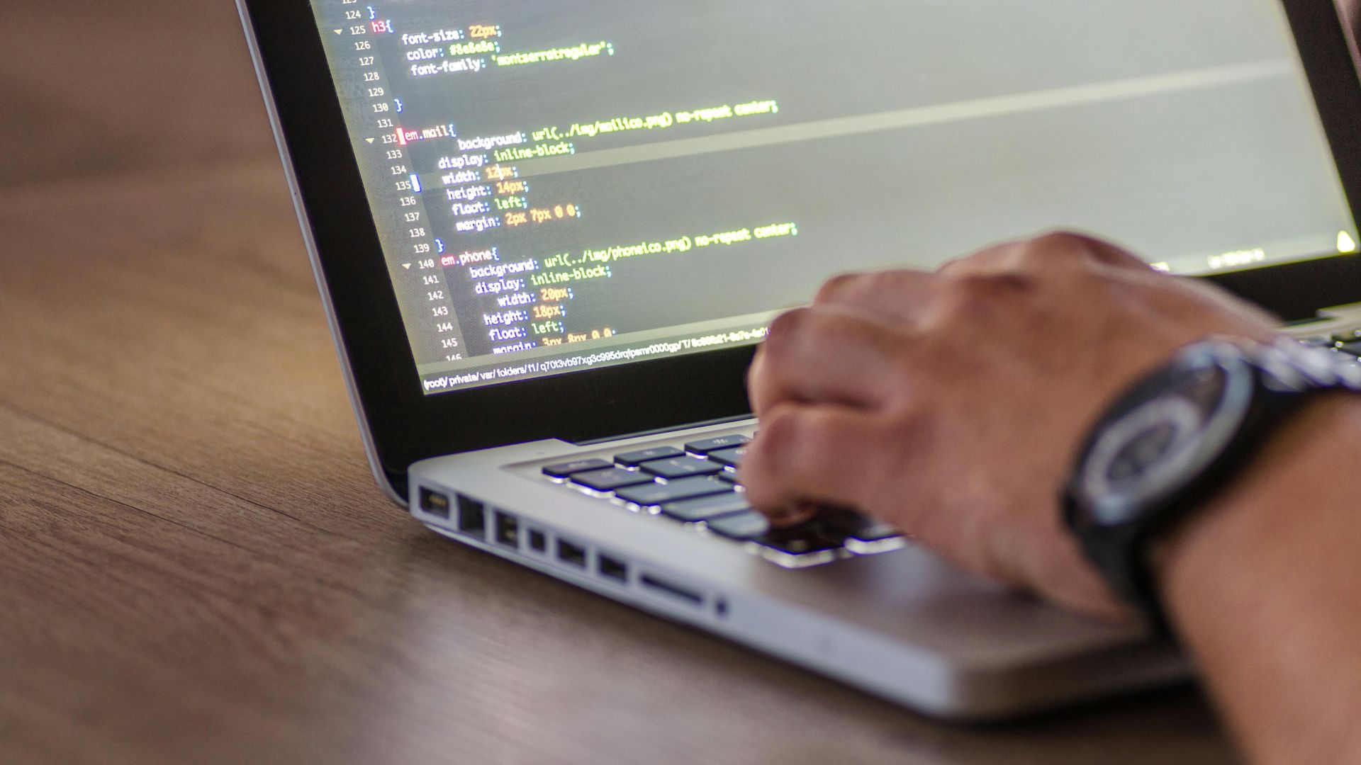Una persona está programando en una computadora portátil con código visible en la pantalla.