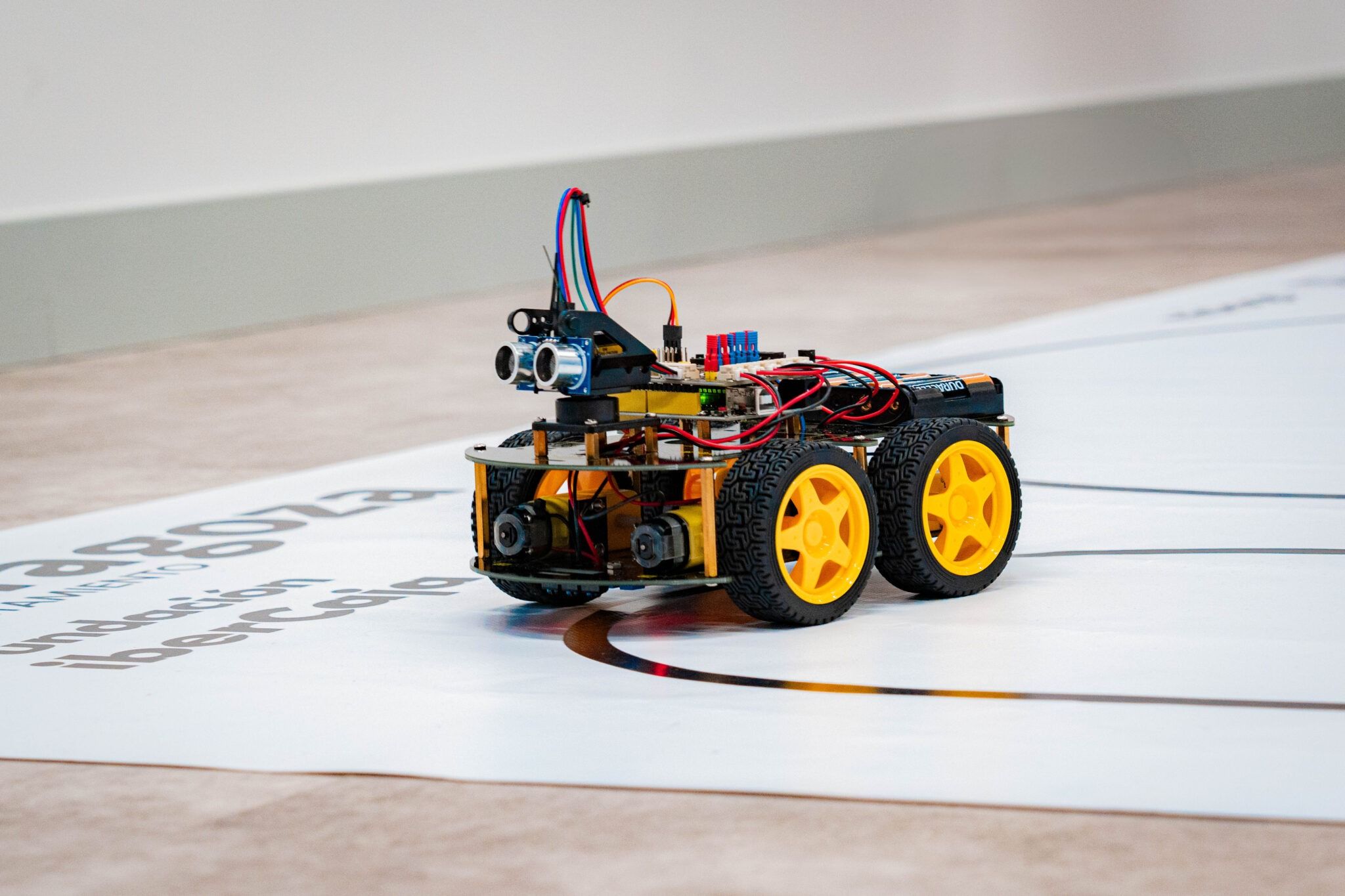 Un robot móvil con ruedas amarillas, equipado con sensores y cables, se encuentra sobre una superficie marcada.
