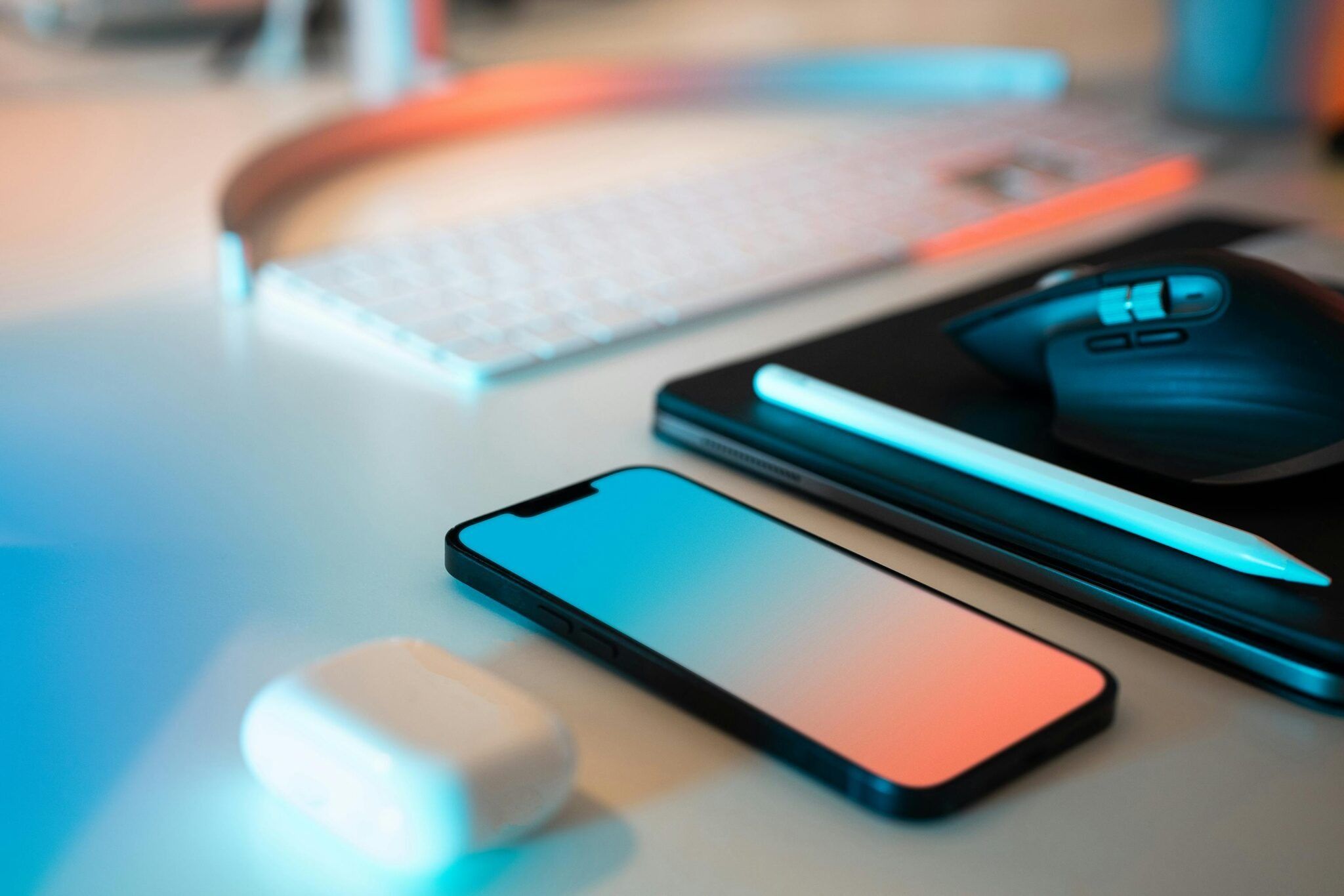 Una imagen de una mesa de trabajo con un teléfono móvil, un ratón, un teclado, unos auriculares y un lápiz óptico.