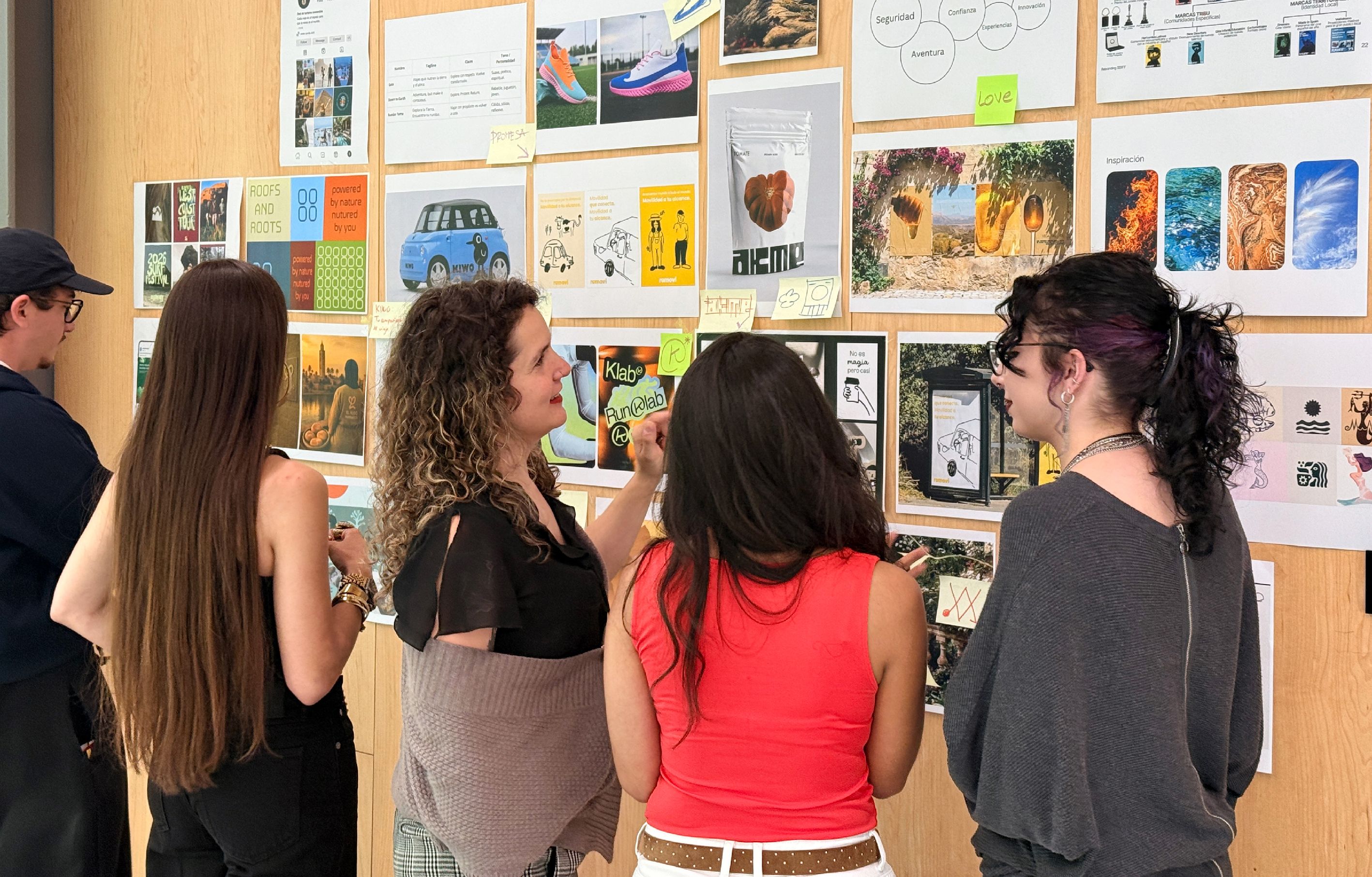 Un grupo de personas observa y comenta un collage de imágenes y diseños en una pared.