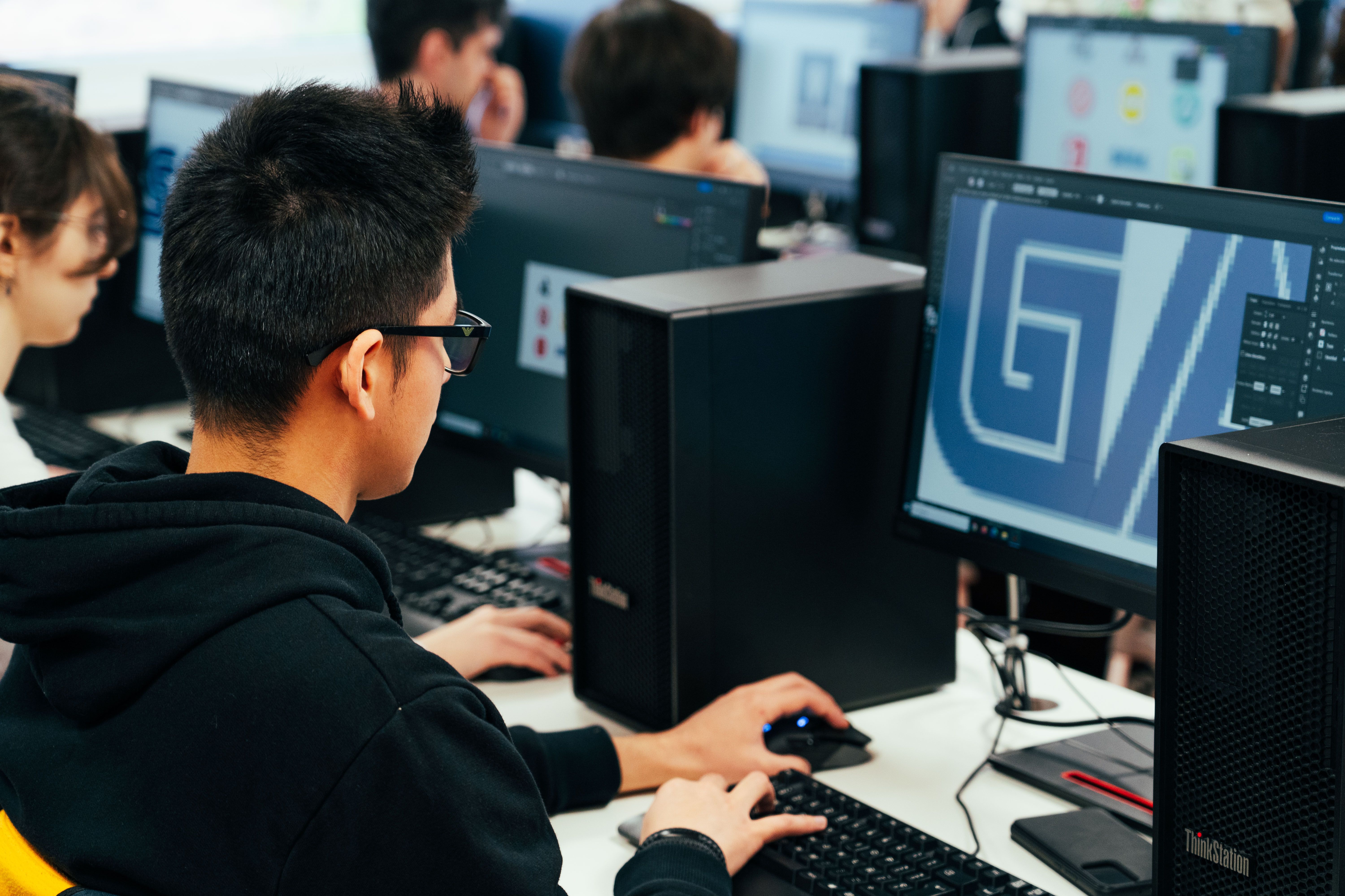 Un grupo de estudiantes trabaja en computadoras en un aula de diseño gráfico.
