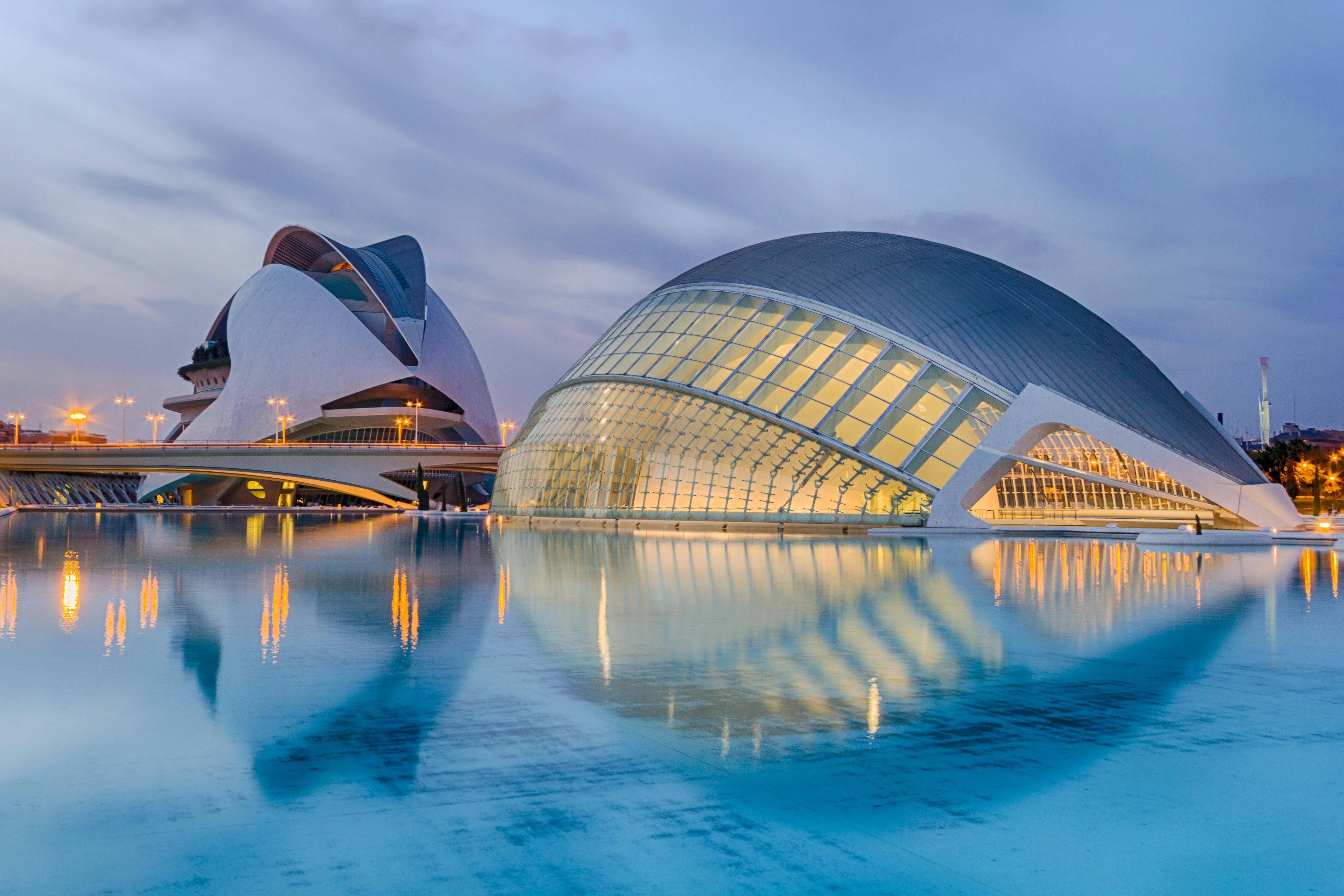 La imagen muestra el emblemático edificio de la Ciudad de las Artes y las Ciencias en Valencia, con sus modernas estructuras y reflejos en el agua al atardecer