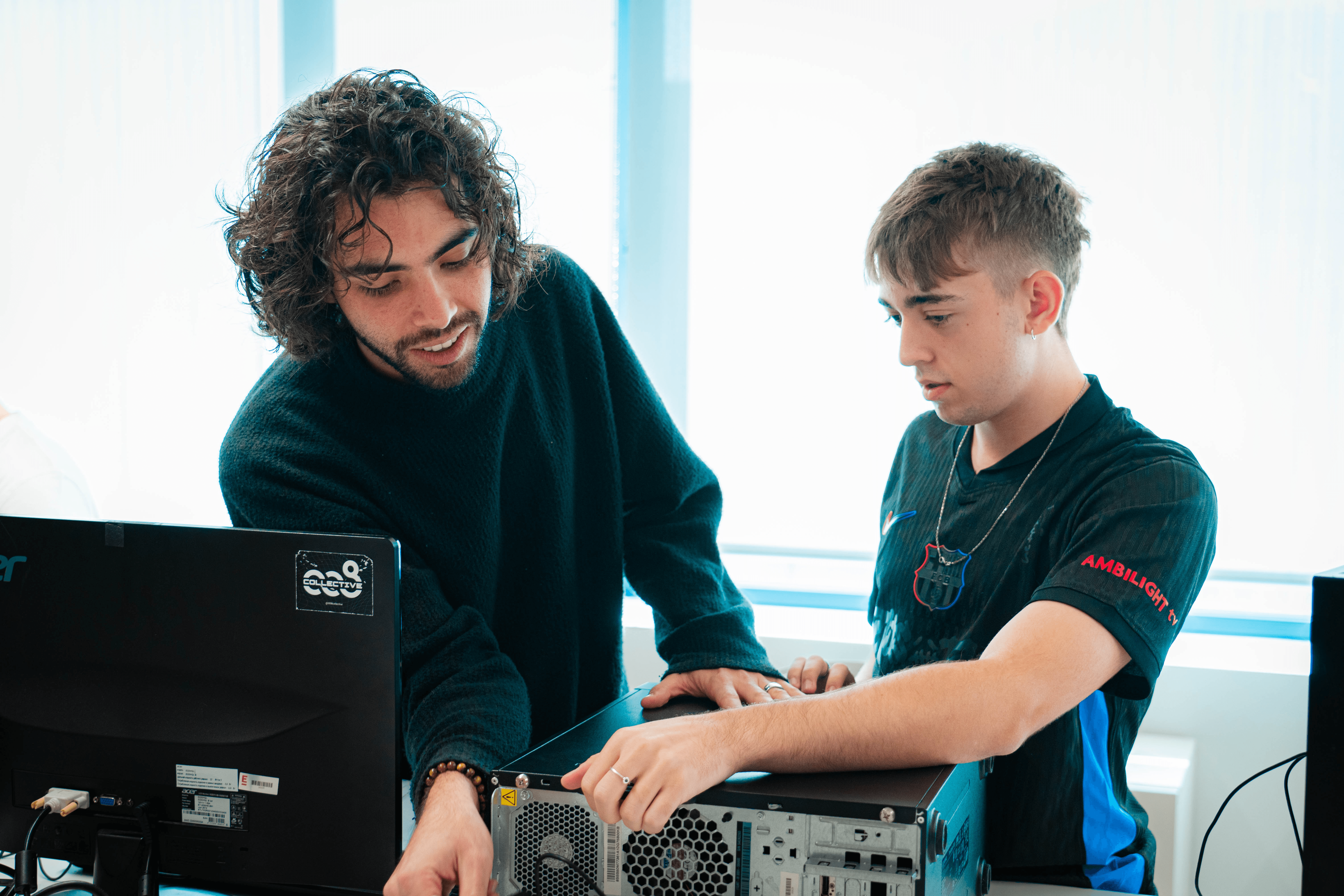 Dos jóvenes trabajan juntos en la parte trasera de una computadora de escritorio.